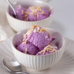 square crop of tow bowls of ube ice cream with toasted coconut and spoons.