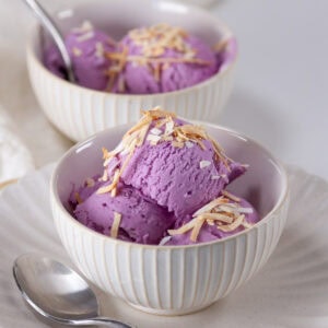 square crop of tow bowls of ube ice cream with toasted coconut and spoons.