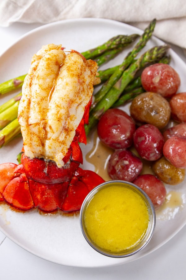 a lobster tail, veggies, and a ramekin of butter sauce on a white plate.