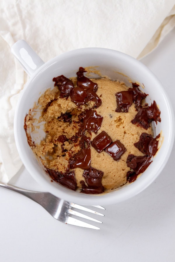 a vanilla mug cake with chocolate chunks and a fork next to it.