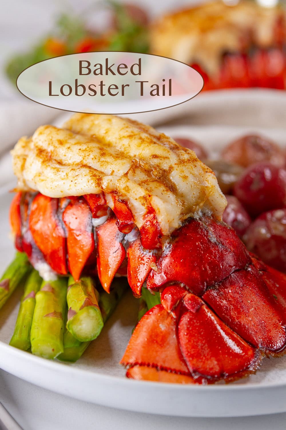 baked lobster tail on roasted asparagus with small potatoes next to it on a white plate.