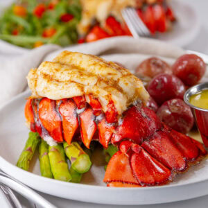 square crop of a baked lobster tail on a plate with all the fixings.