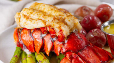 square crop of a baked lobster tail on a plate with all the fixings.
