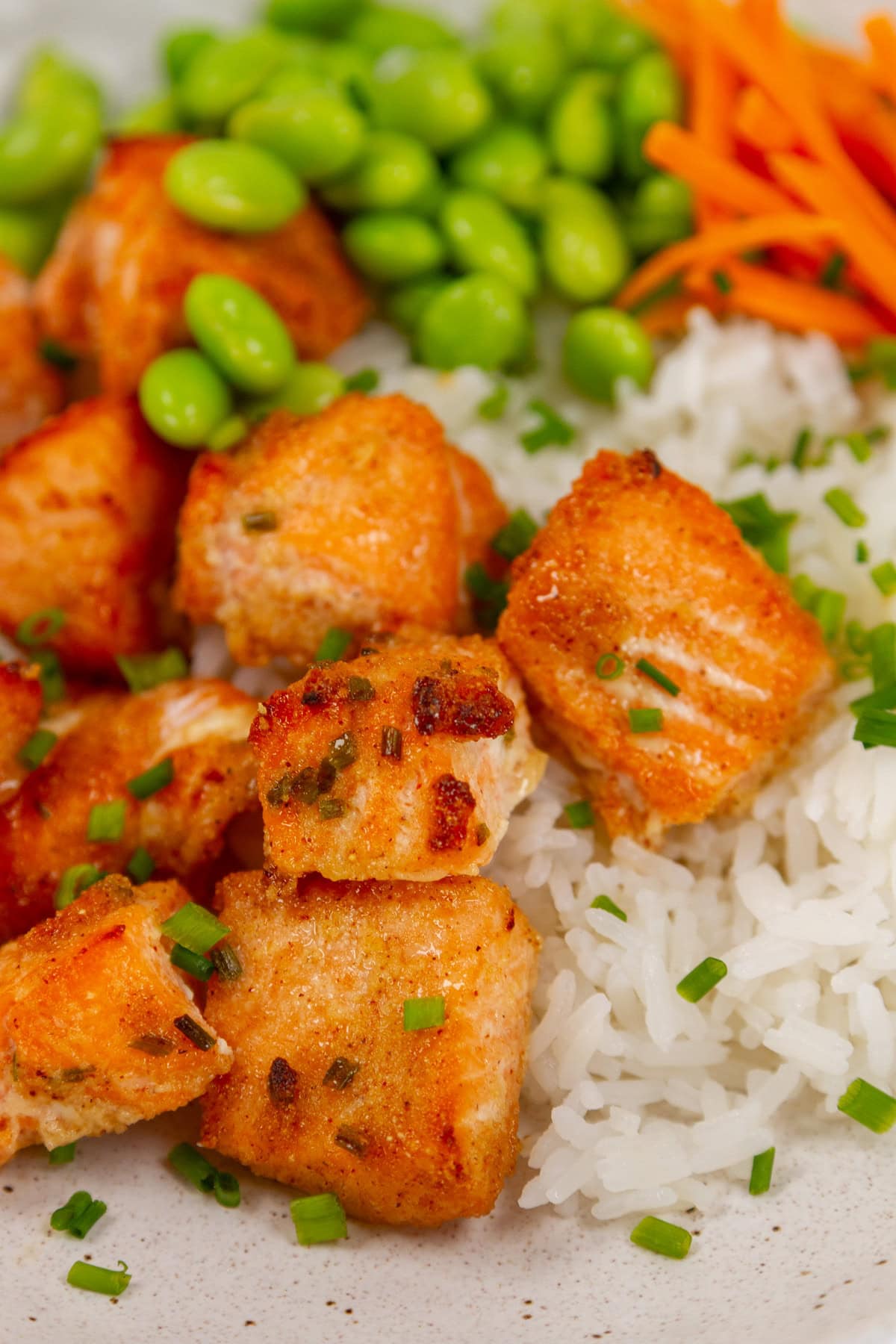 salmon bites on rice with edamame and carrots.