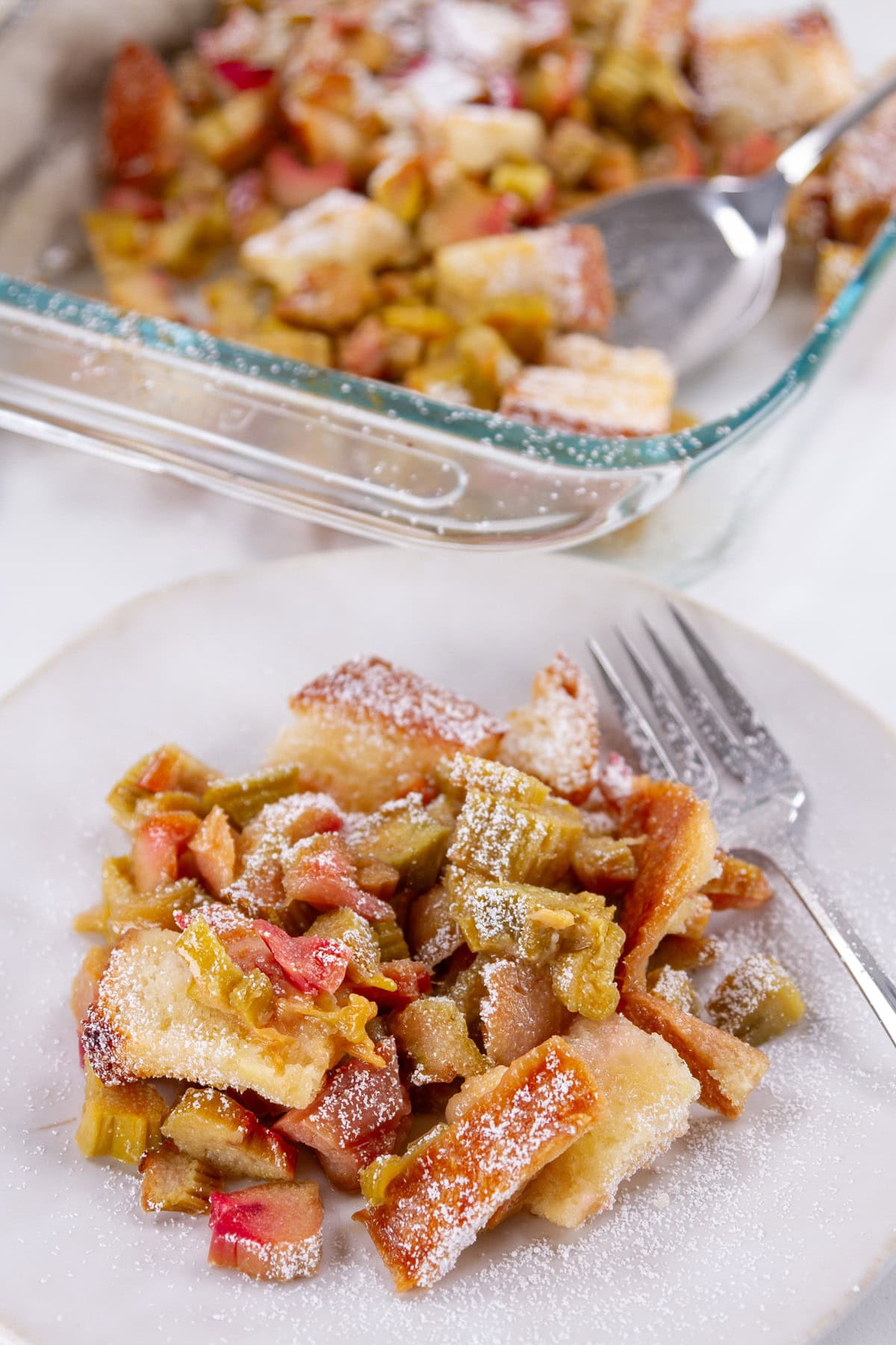 a serving of baked bread pudding with rhubarb on a plate in front of the baking dish.