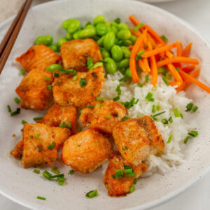 square crop of cooked salmon cut into cubes on rice with edamame and carrots.