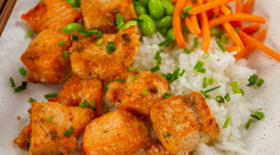 square crop of cooked salmon cut into cubes on rice with edamame and carrots.