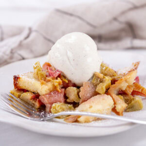 square crop of a serving of rhubarb dessert with vanilla ice cream and a fork in front of it.