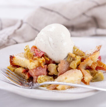 square crop of a serving of rhubarb dessert with vanilla ice cream and a fork in front of it.