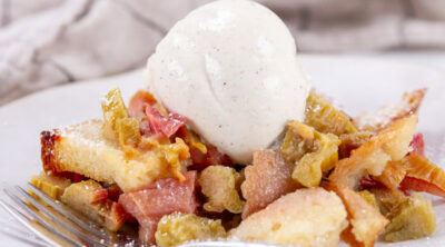 square crop of a serving of rhubarb dessert with vanilla ice cream and a fork in front of it.
