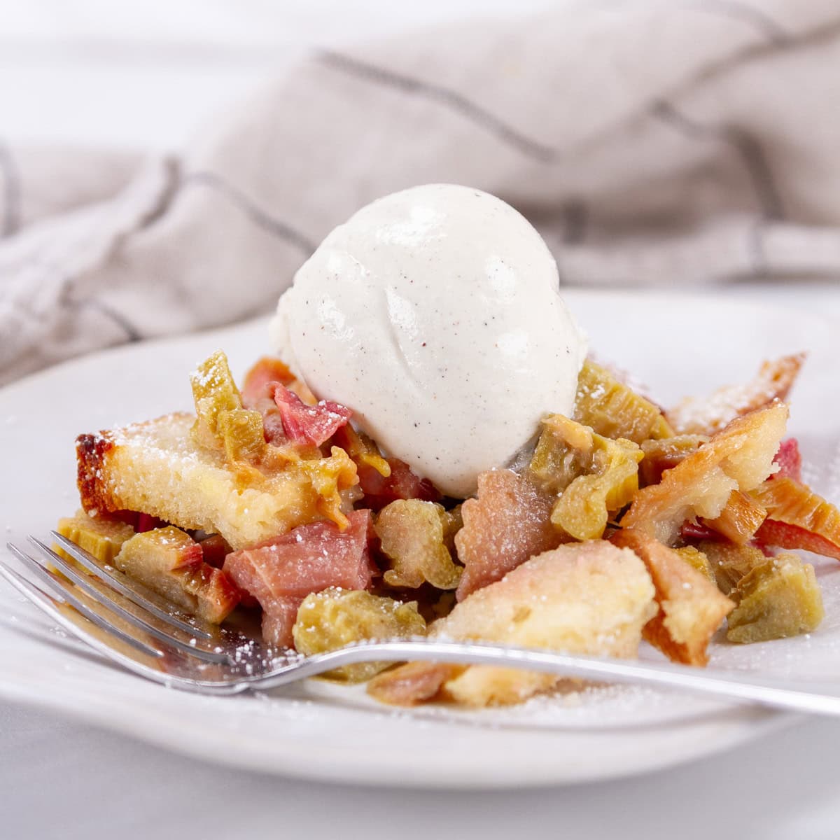 square crop of a serving of rhubarb dessert with vanilla ice cream and a fork in front of it.
