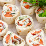square crop of several pinwheel appetizers filled with cream cheese and salmon, and there's fresh parsley in the upper right.