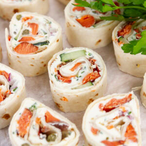 square crop of several pinwheel appetizers filled with cream cheese and salmon, and there's fresh parsley in the upper right.