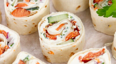 square crop of several pinwheel appetizers filled with cream cheese and salmon, and there's fresh parsley in the upper right.