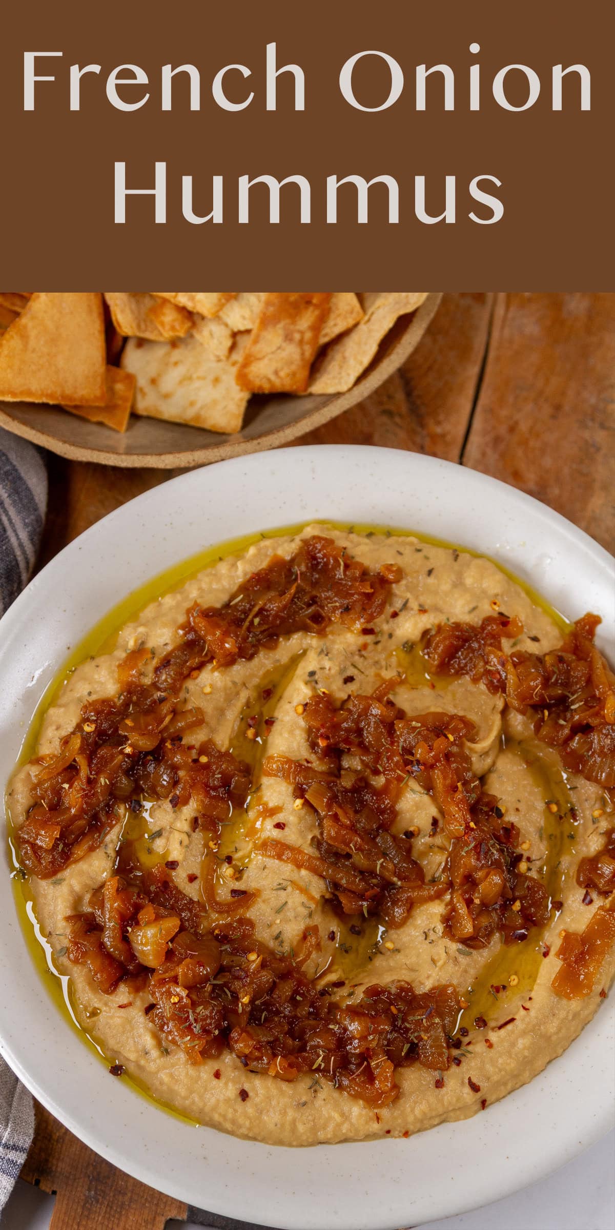 a bowl of hummus with caramelized onions on top, pita chips in the upper left.