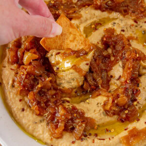 square crop of dipping a pita chip into hummus.