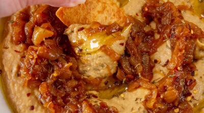 square crop of dipping a pita chip into hummus.