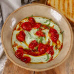 square crop of a bowl of ricotta topped with tomatoes, oil, and basil.