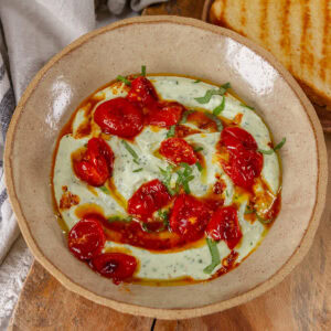 square crop of a bowl of ricotta topped with tomatoes, oil, and basil.