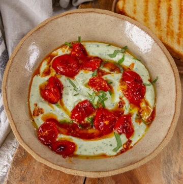 square crop of a bowl of ricotta topped with tomatoes, oil, and basil.