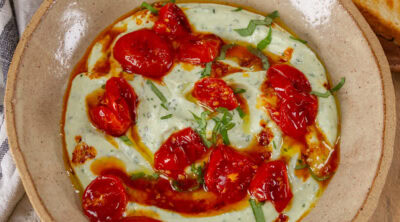 square crop of a bowl of ricotta topped with tomatoes, oil, and basil.