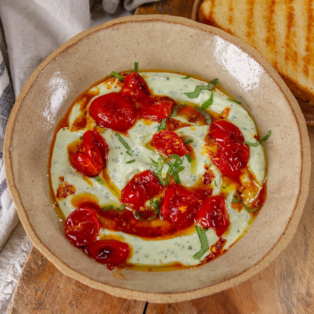 square crop of a bowl of ricotta topped with tomatoes, oil, and basil.