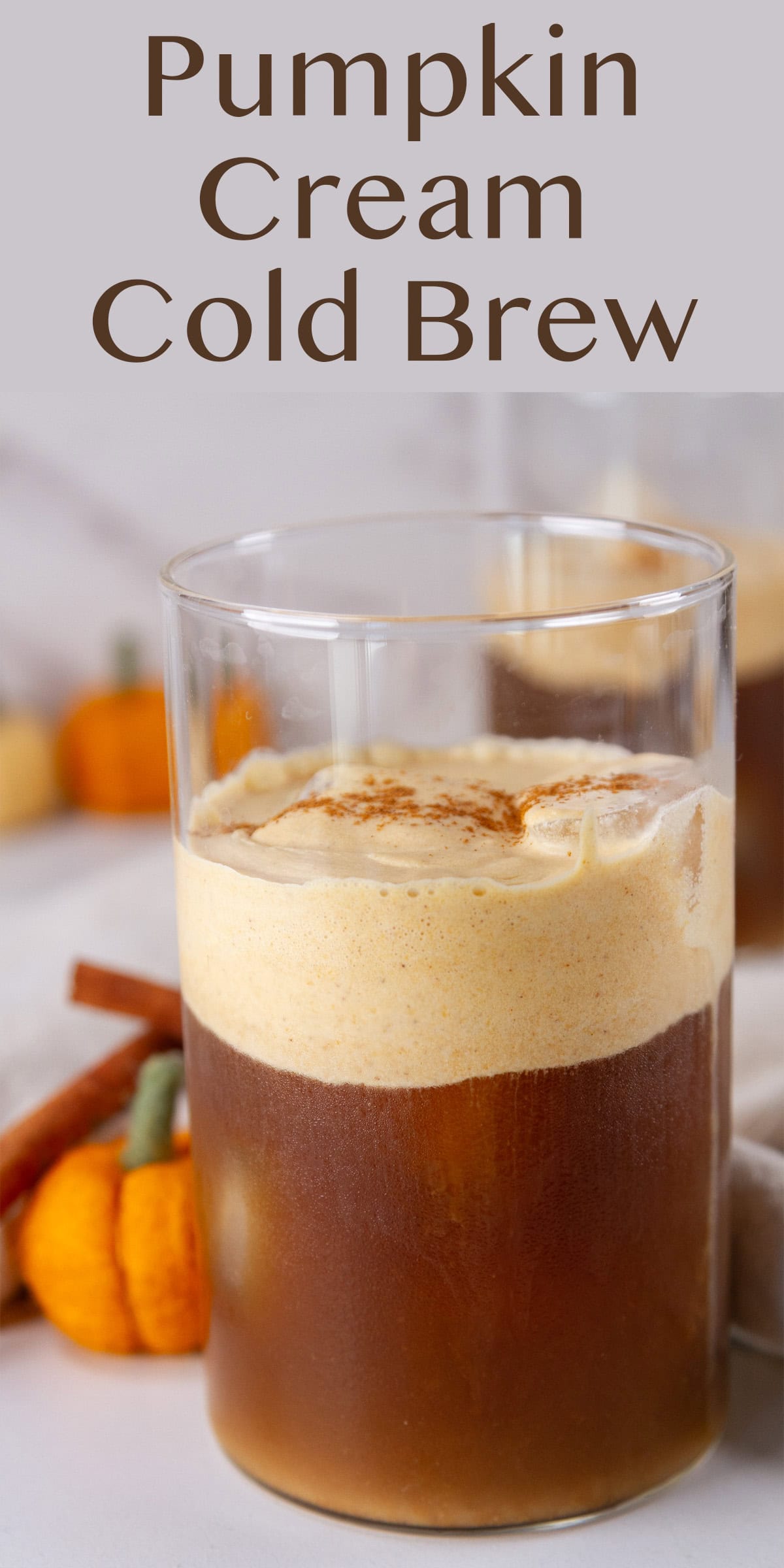 a glass of iced coffee with cold foam in front of cinnamon sticks and a felted pumpkin.