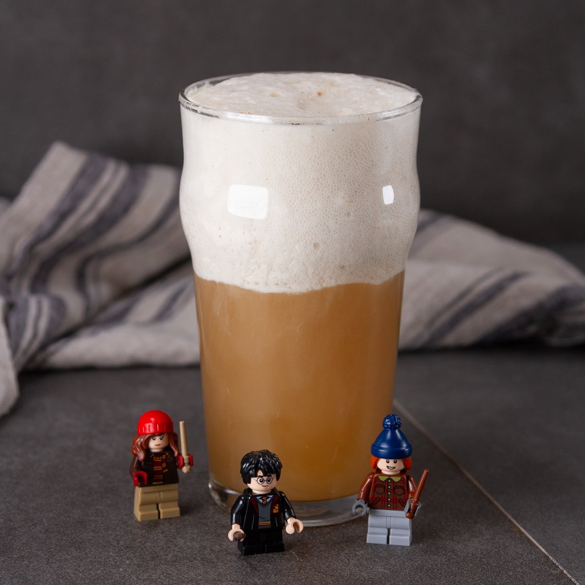 square crop of a glass of butterbeer with Lego Harry Potter figures around it.
