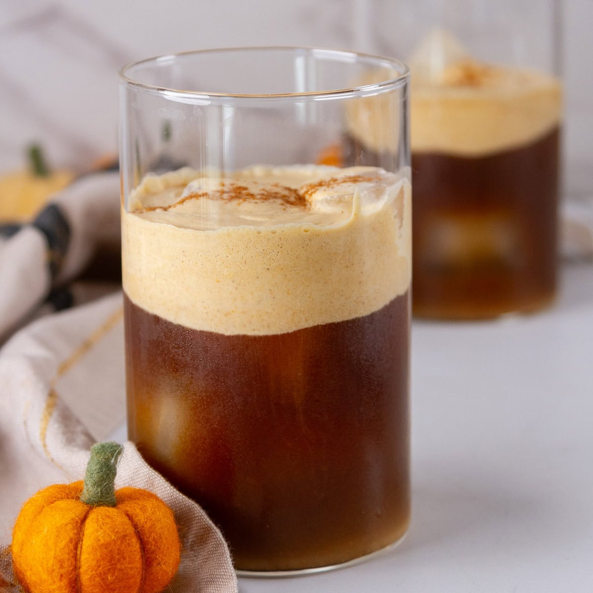 square crop of two glasses of iced coffee with pumpkin cold foam on top.