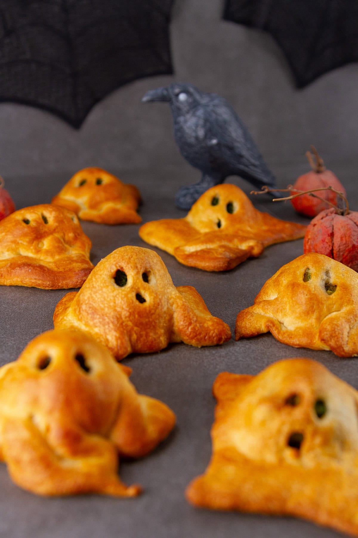 crescent roll ghosts on a black background with a Halloween crow in the back.