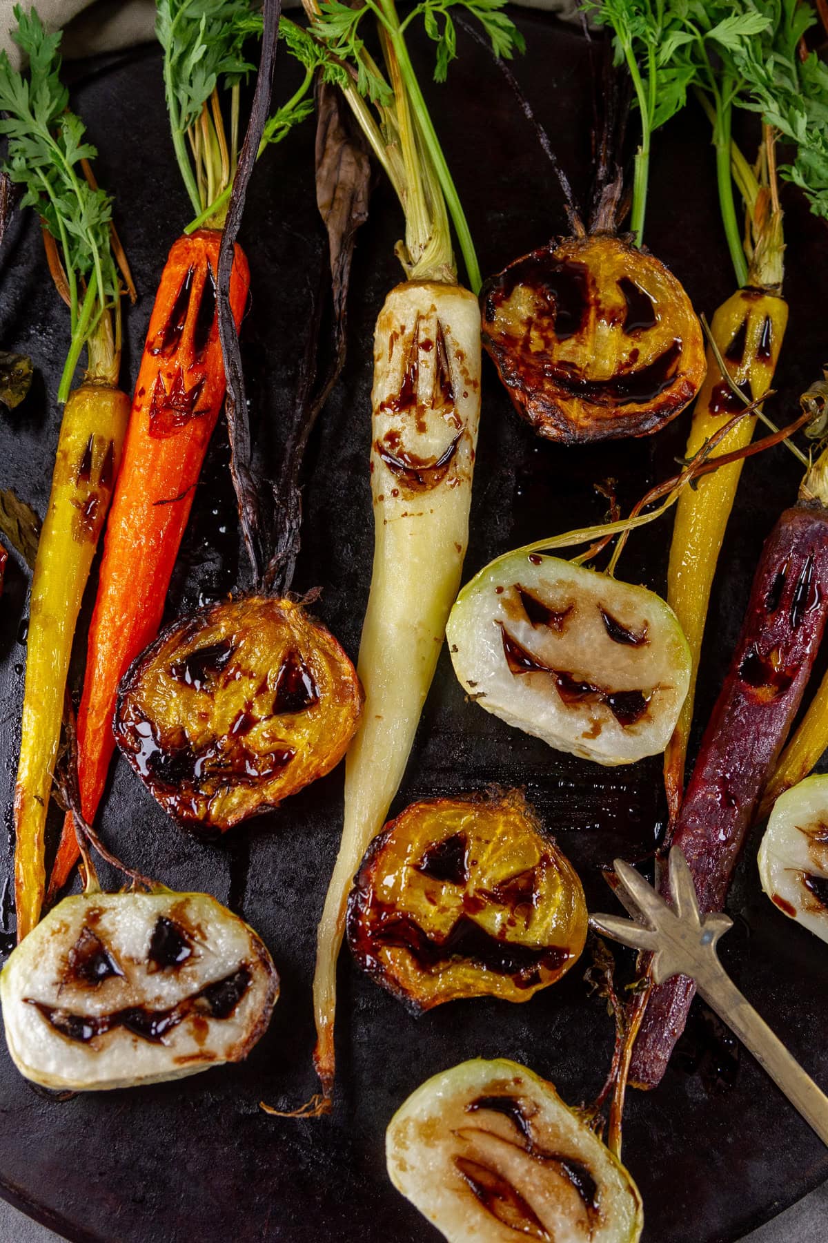 a bunch of veggies with carved Halloween faces on a black serving tray.