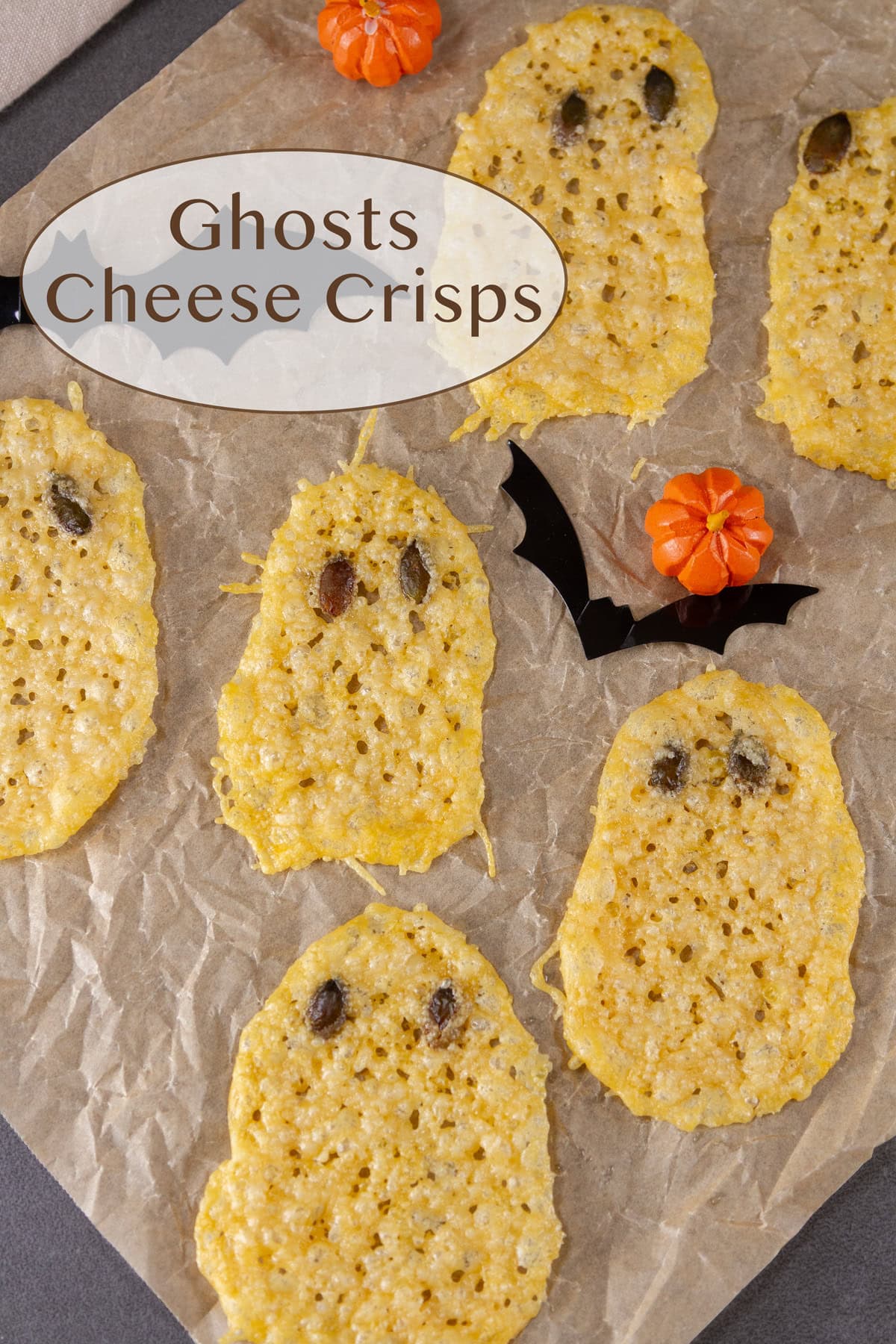 several cheese crisps shaped like ghosts on a piece of parchment peper with Halloween decorations around.
