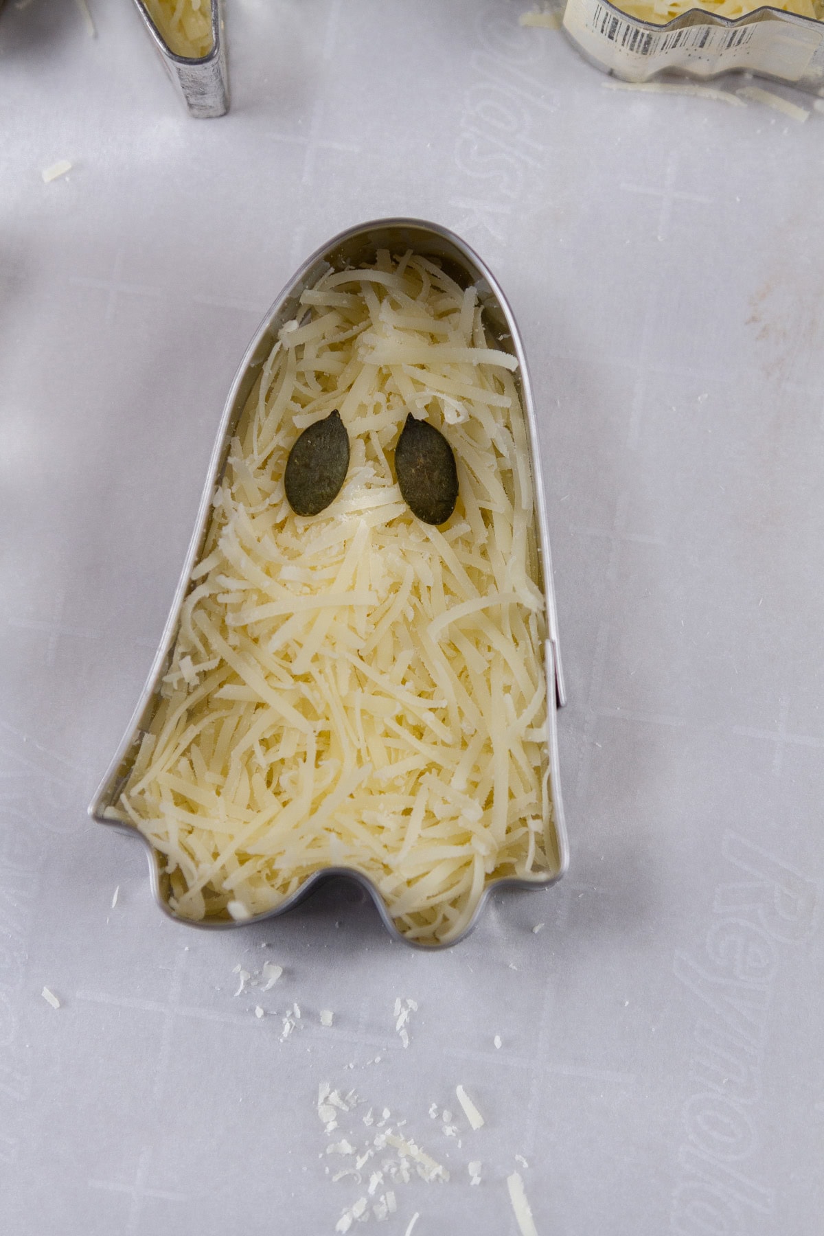 a ghost cookie cutter filled with shredded cheese and pumpkin seeds for eyes.