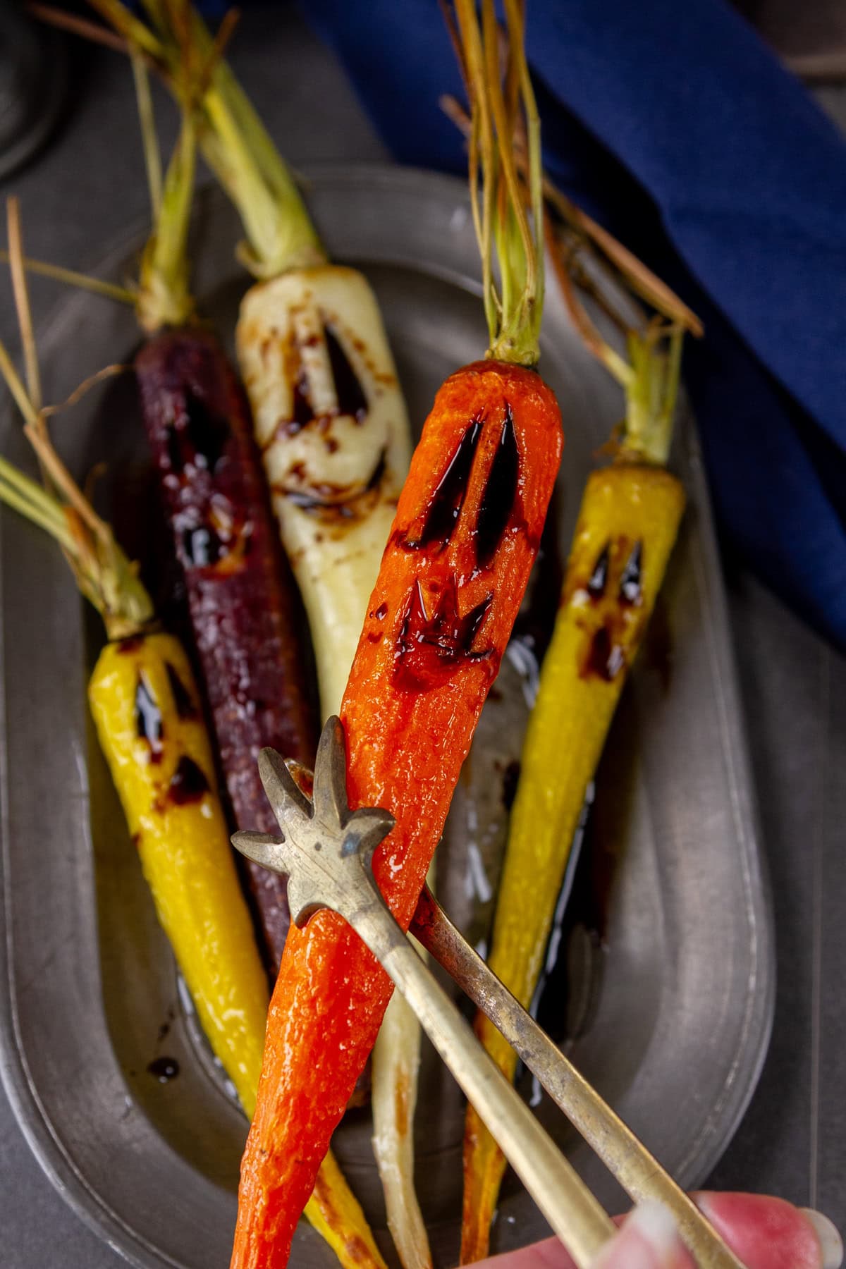 a carrot being picked up by tongs in front of the pewter tray of carrots.
