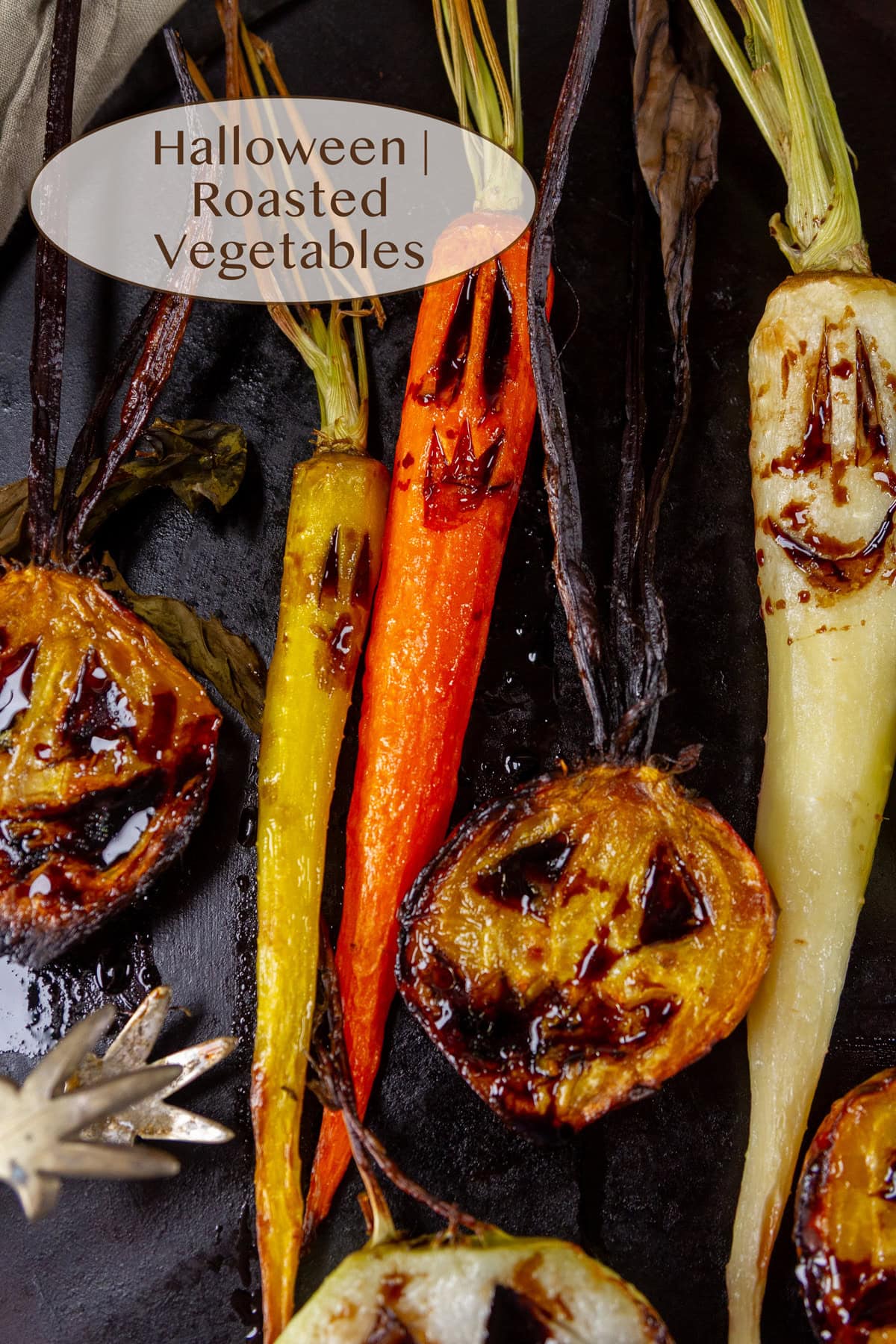 roasted vegetables with Halloween faces on a black serving tray.