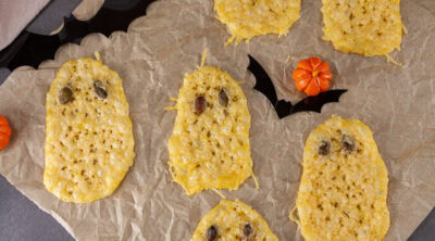 square crop of several cheese crisps shaped like ghosts on parchment paper.