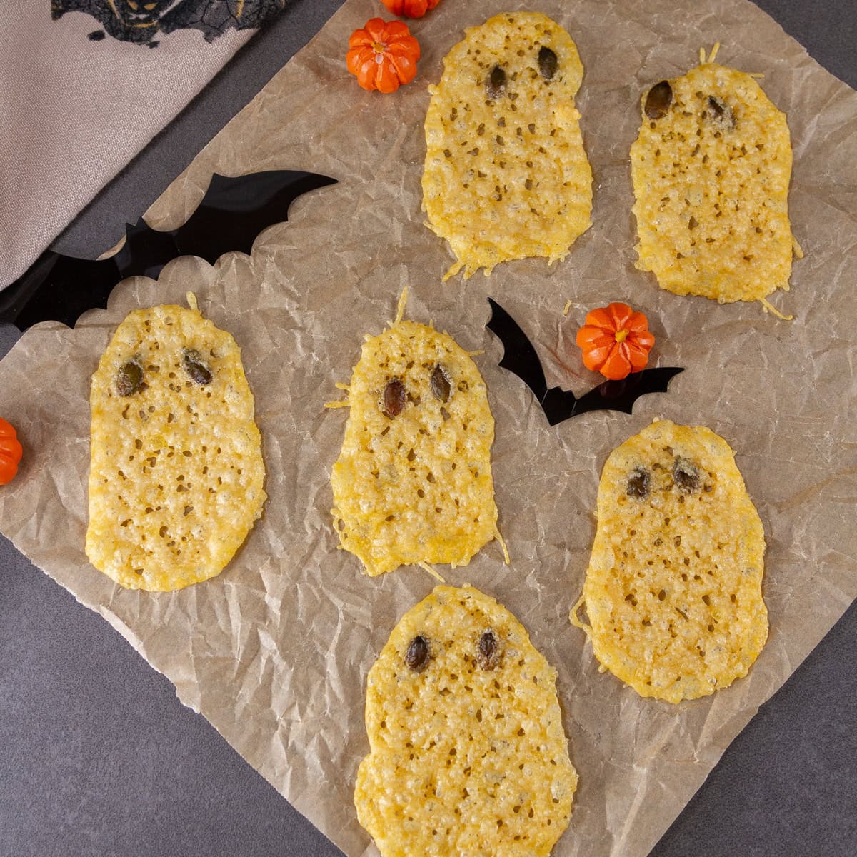 square crop of several cheese crisps shaped like ghosts on parchment paper.