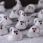 square crop of a bunch of ghost shaped marshmallows on powdered sugar on a black background.