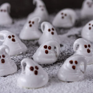 square crop of a bunch of ghost shaped marshmallows on powdered sugar on a black background.