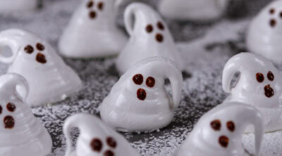 square crop of a bunch of ghost shaped marshmallows on powdered sugar on a black background.
